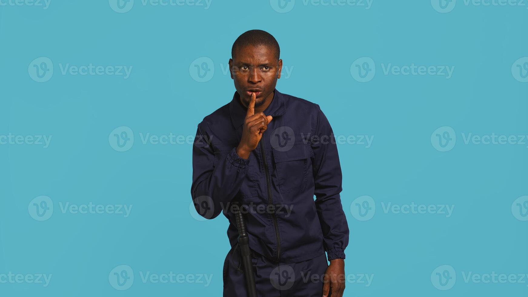 Security guard doing shush sign gesturing with finger, preventing public access in restricted area. Portrait of stern bodyguard urging people to keep quiet, studio background, camera B photo