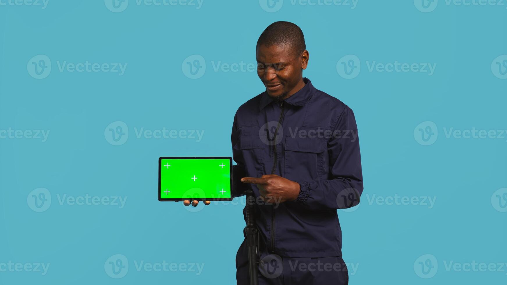 Portrait of happy security staff member showing isolated screen tablet. Joyous patrolling agent maintains secure environment, showcasing chroma key device, studio background, camera B photo