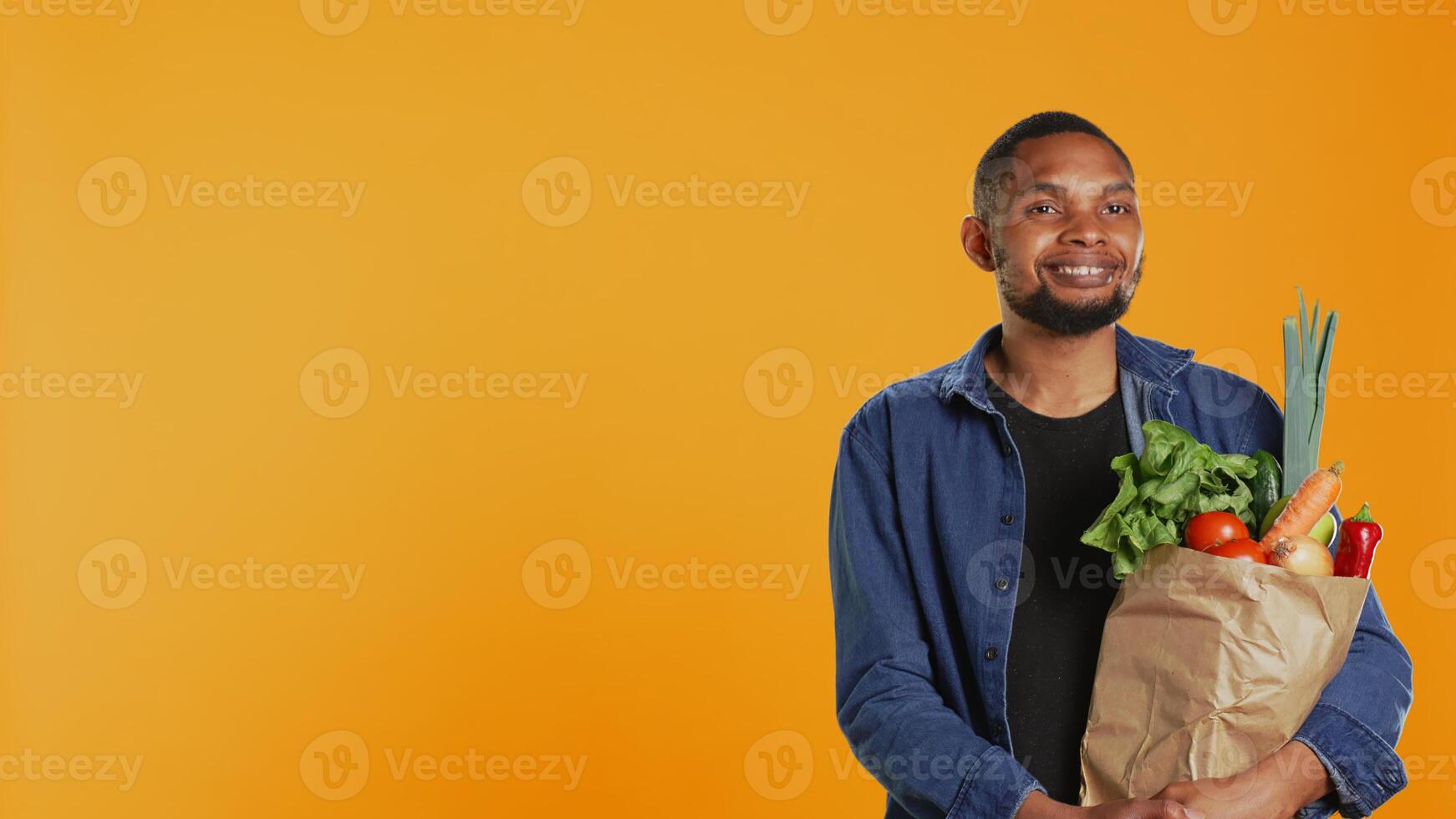 Portrait of african american guy posing with a paper bag full of groceries, shopping for organic ethically sourced goods. Vegan person supporting zero waste sustainable lifestyle. Camera B. photo