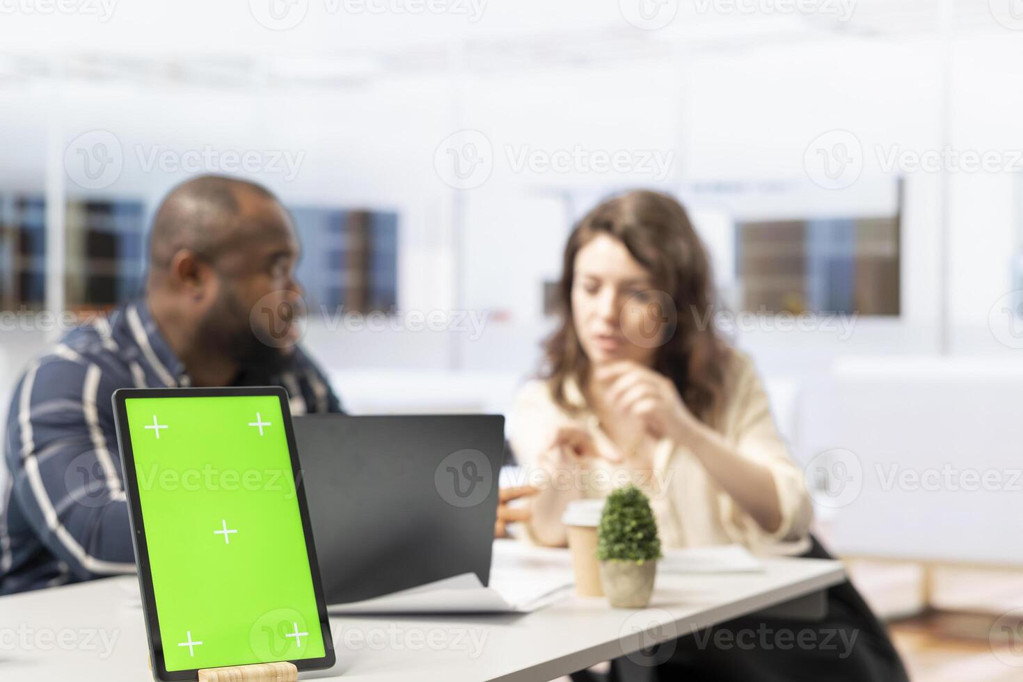 Businessman meets with woman realtor regarding an office tour, discussing at desk next to chroma key mockup. Contractor presenting high class office space blueprints for renting. photo