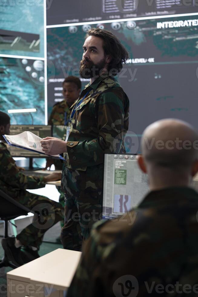 Army IT professional supervising data collecting activity from a big screen, processing strategic information to create a new map for field operations. Military defense program in control room. photo