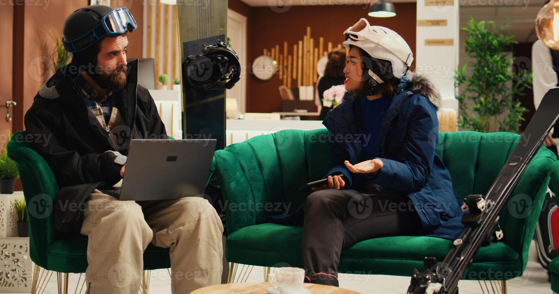Focused couple using gadgets in lobby, arriving at ski lodging during wintertime season. Man searches for slope activity online while woman checks social media messages. Handheld shot. photo