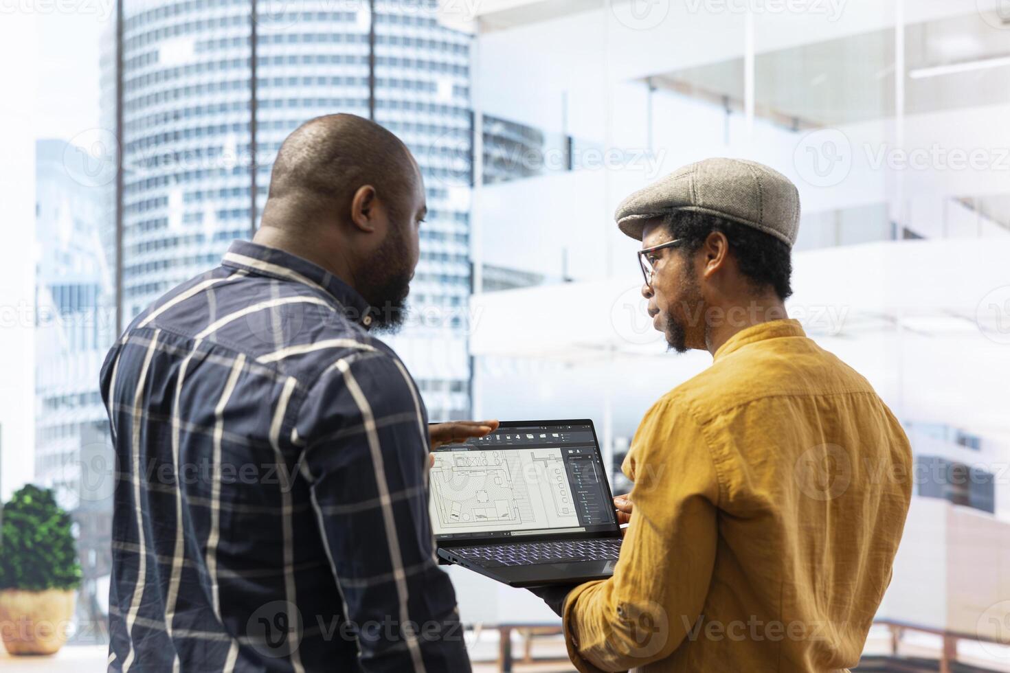 Real estate broker and client negotiating a leasing contract for a high class modern office space, evaluating blueprints on laptop during office tour. Property investment opportunity. photo