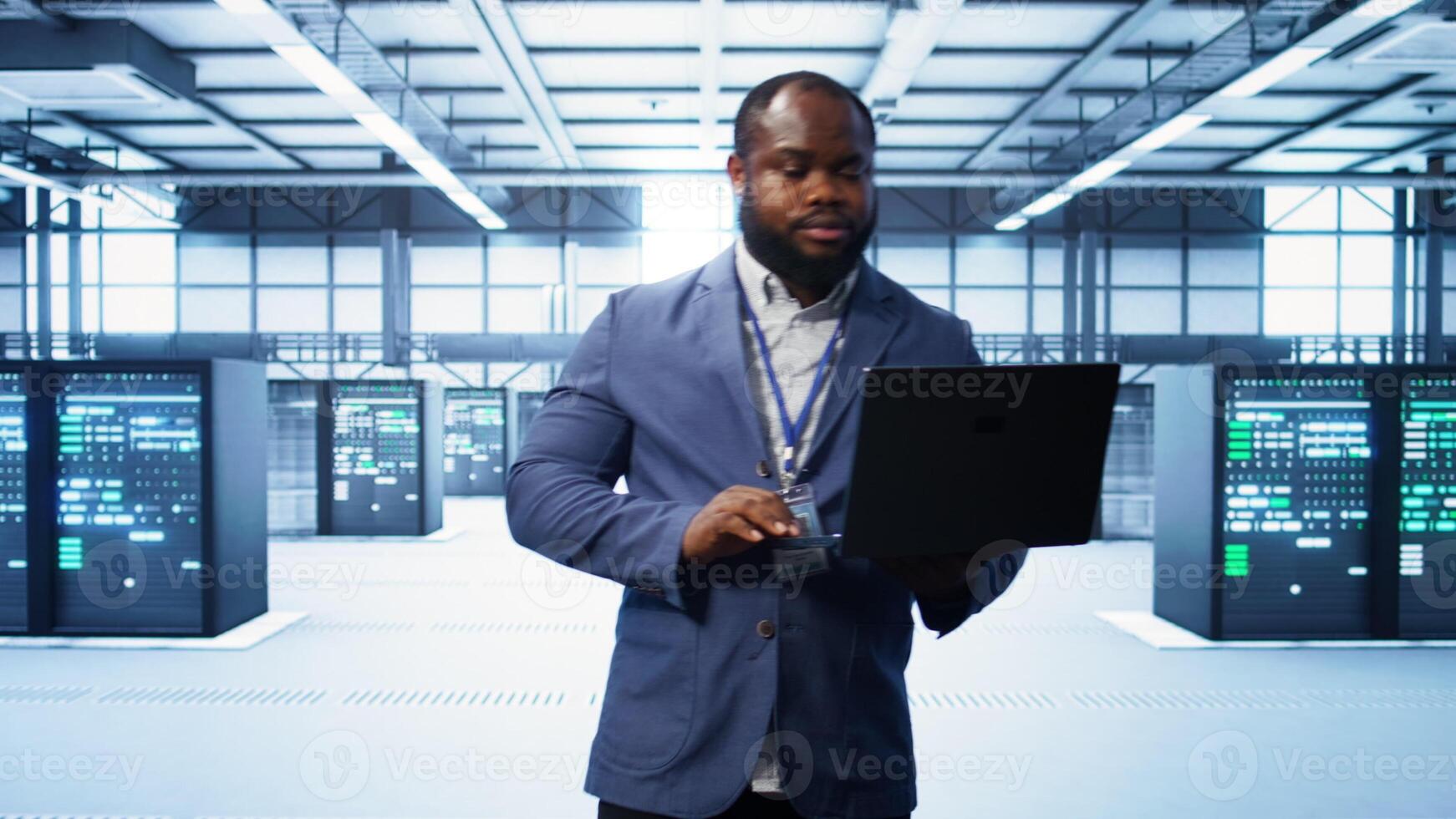 IT engineer working on laptop in modern data center, overseeing server operations, system maintenance,and cybersecurity protocols, ensuring optimal performance and data integrity, camera B photo