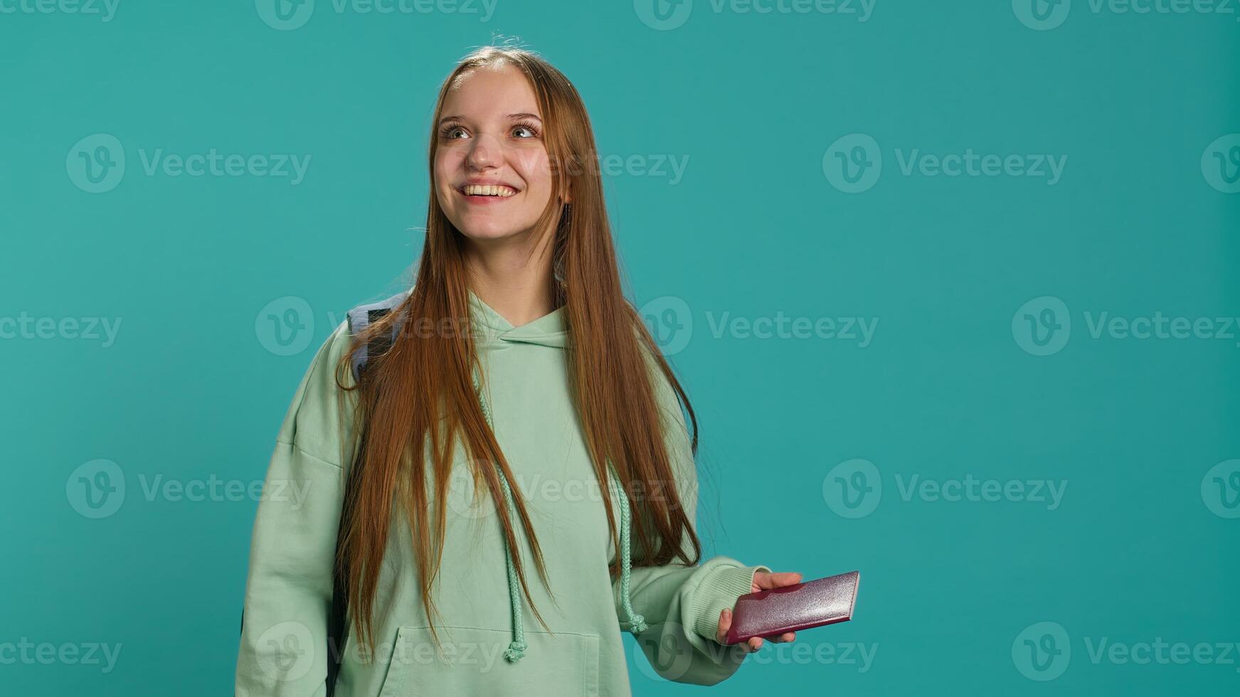 Jolly teenage woman holding passport, going on adventure trip, looking around. Cheerful wanderlust tourist backpacking, sightseeing, visiting attractions, isolated over studio backdrop, camera A photo