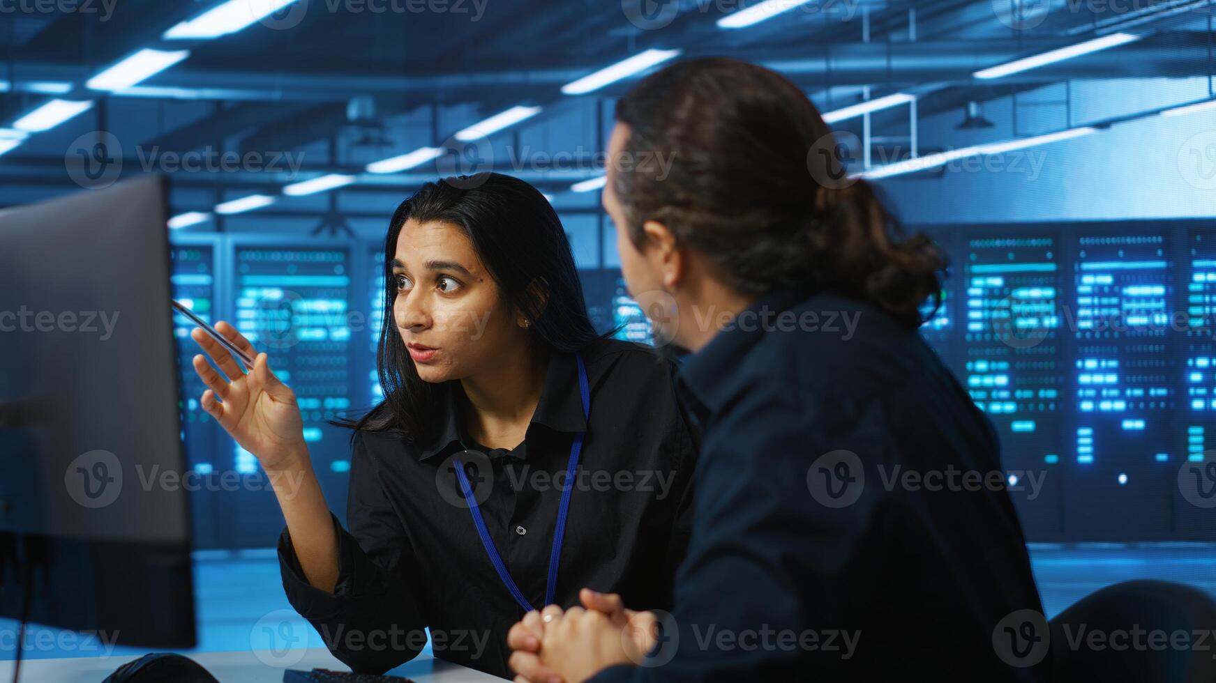 Programmers talking in high tech server hub, using PCs to analyze data. Colleagues examining infrastructure in data center, ensuring system integrity and security, doing brainstorming photo
