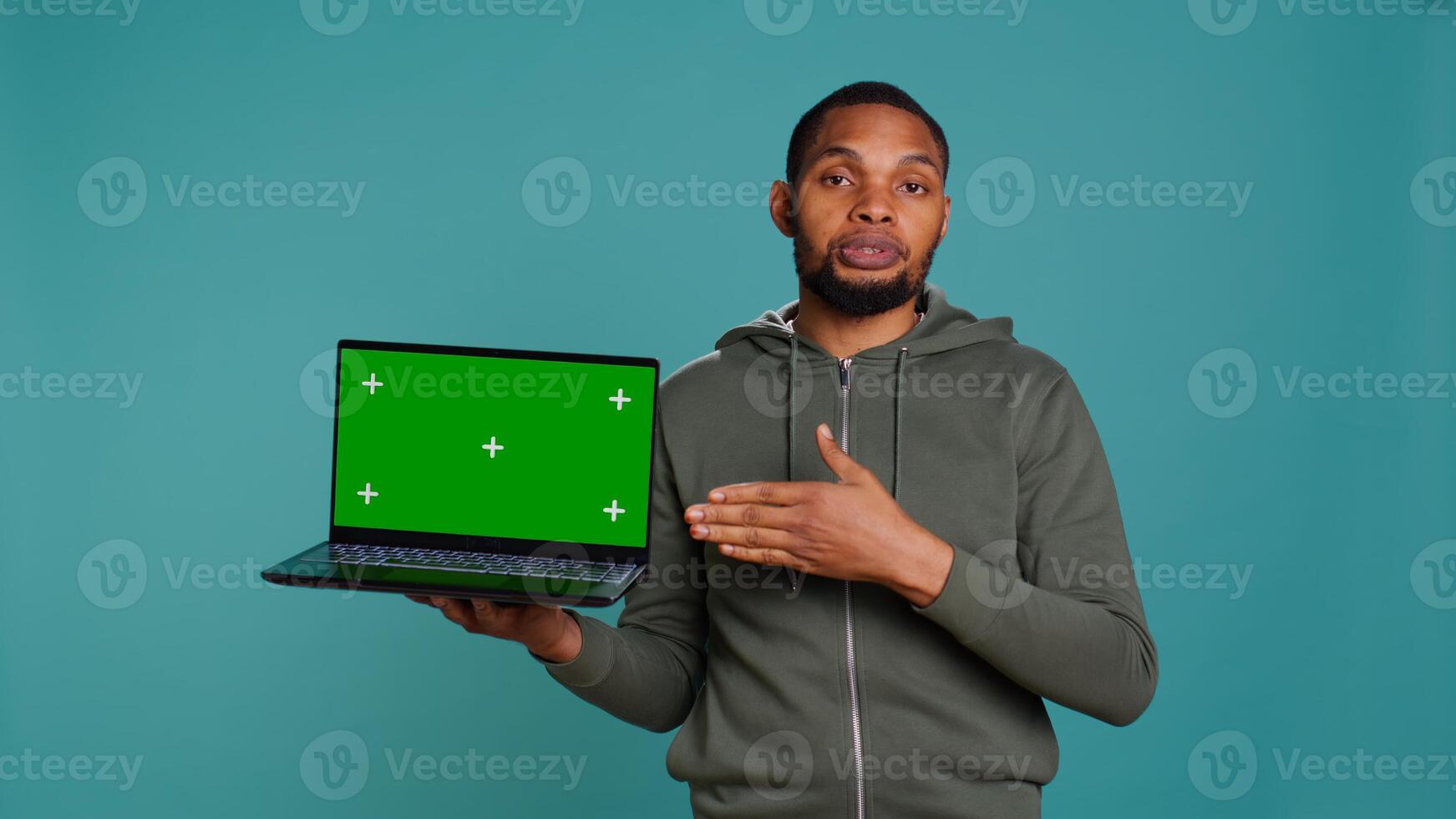 Jolly african american man holding green screen laptop, doing recommendation. Friendly BIPOC person pointing towards mockup notebook, giving positive feedback, studio background, camera B photo