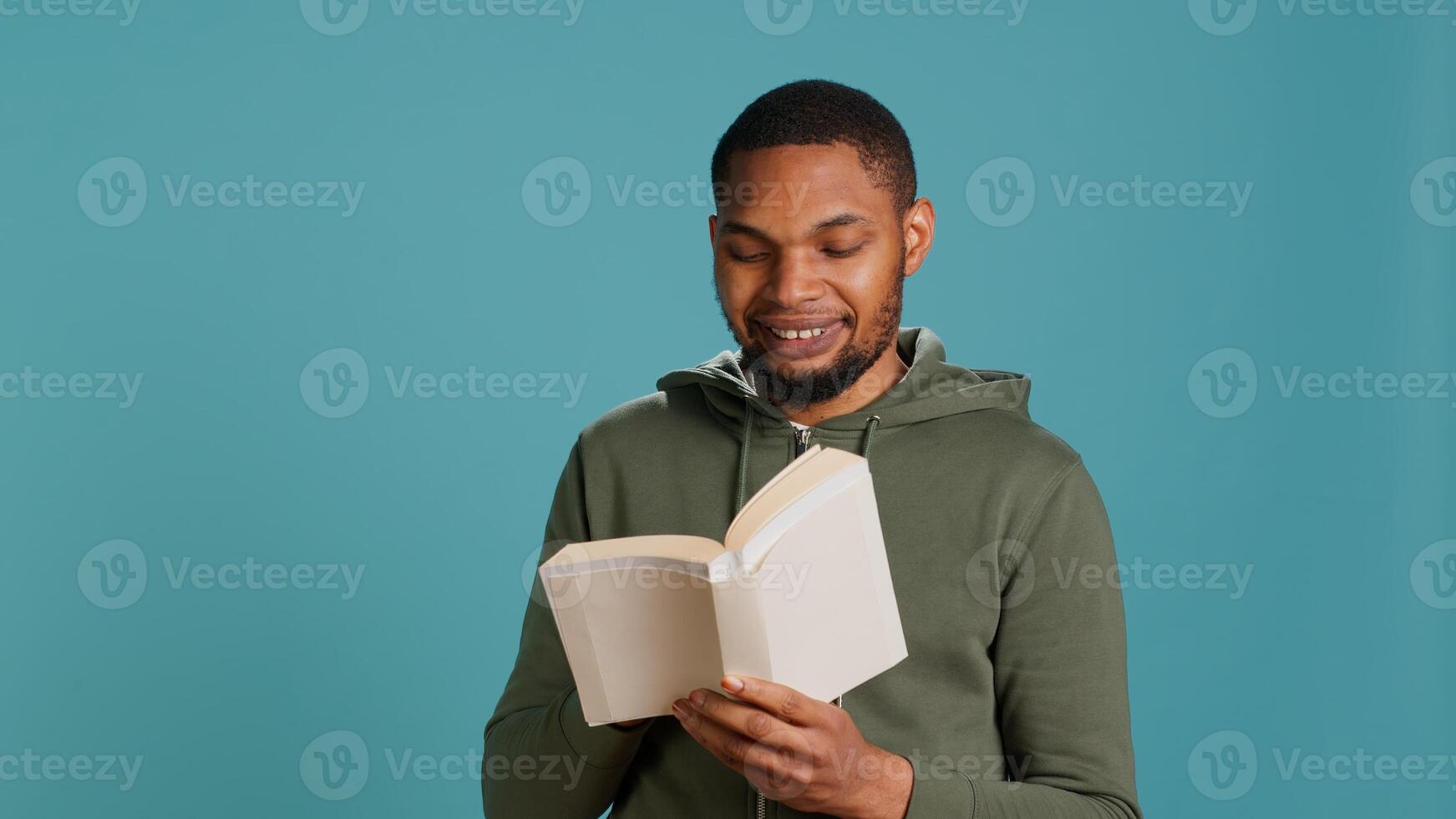 Man laughing while reading funny book, entertained by engrossing story. Joyful person having fun, being amused by literature novel during leisure time in studio background, camera A photo