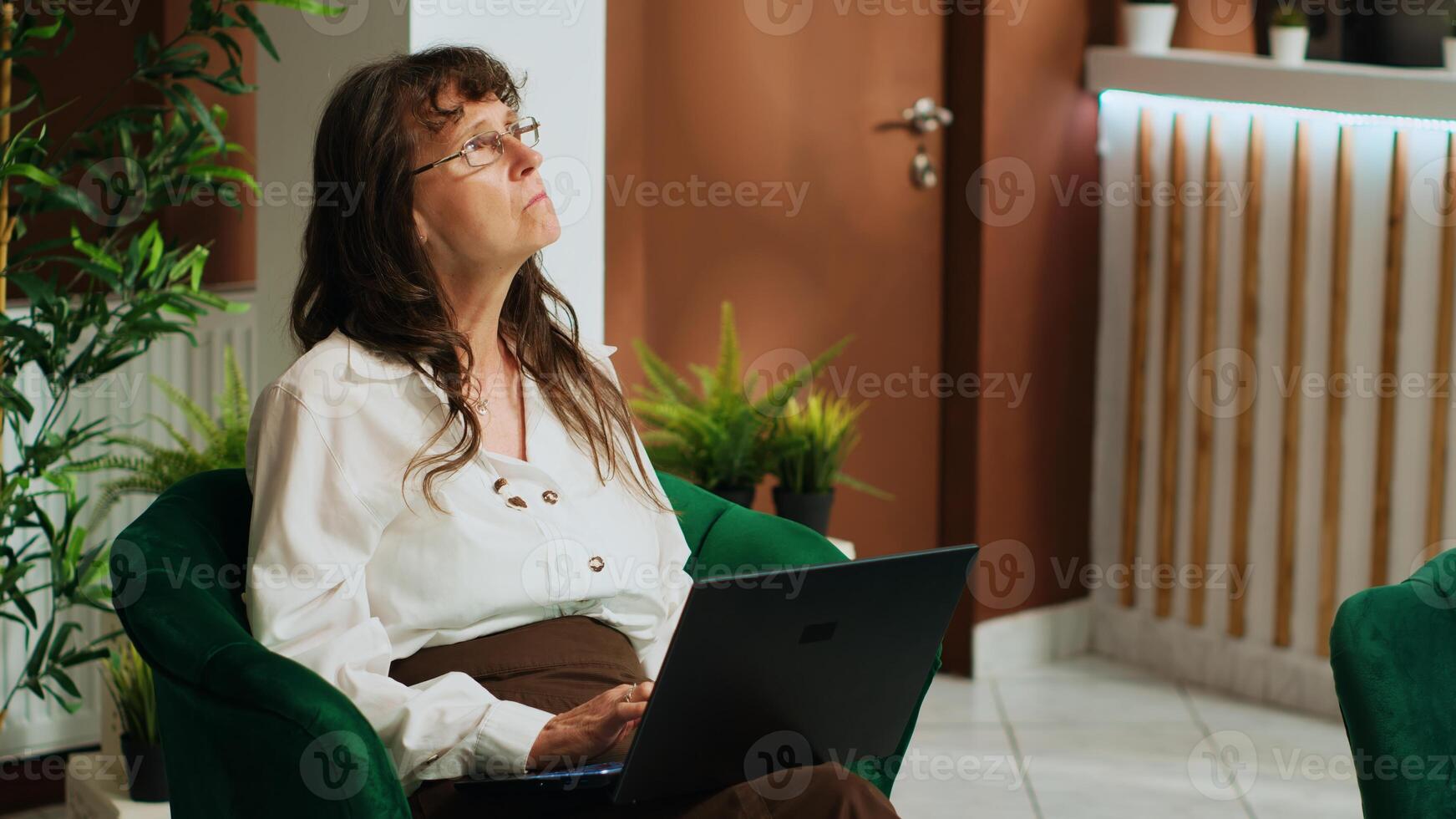 Elderly traveller browsing laptop in lobby, searching for beautiful landmarks to visit while travelling on retirement vacation. Woman waiting in lounge area and checking internet reviews. photo