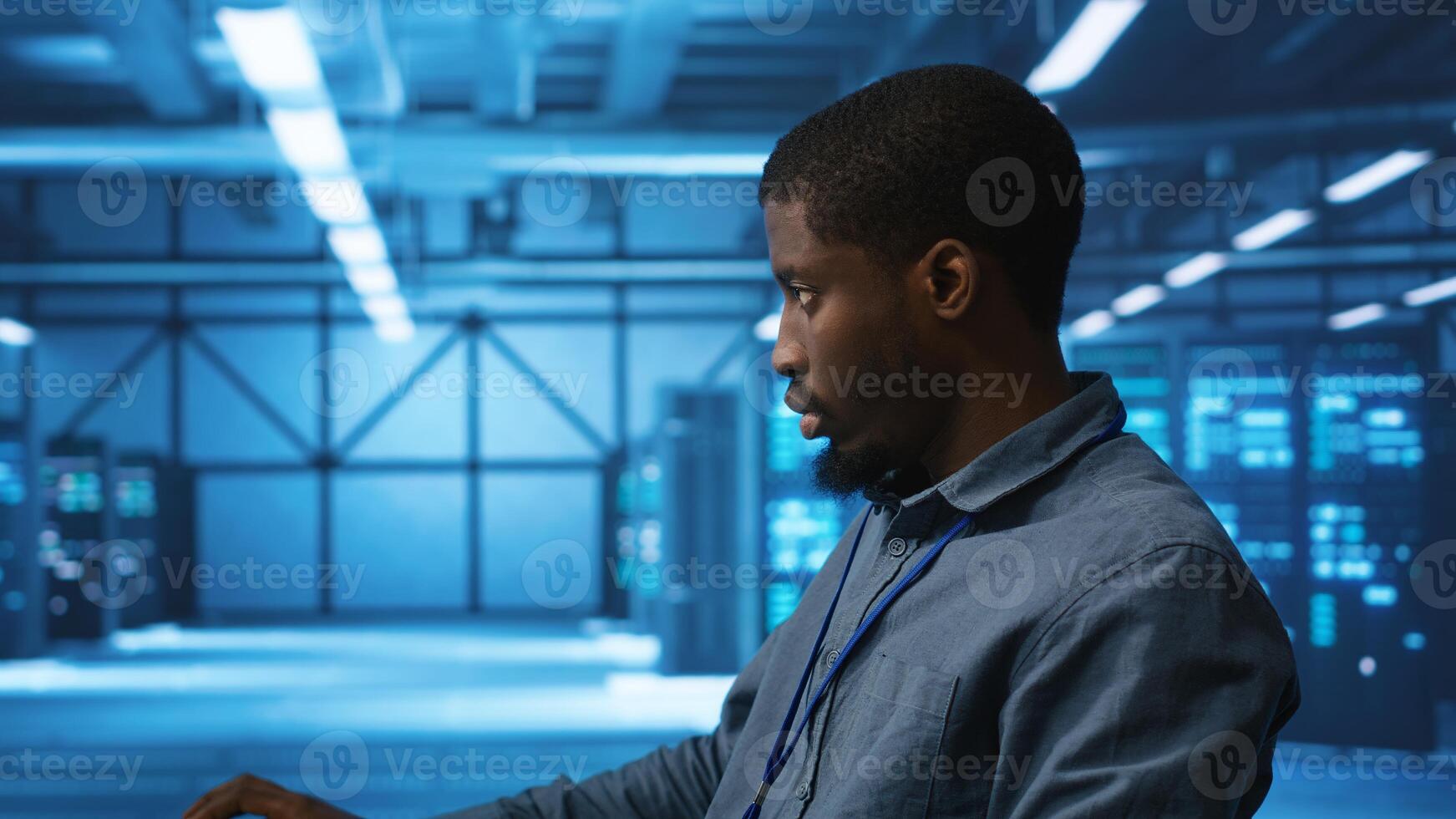 African american IT expert in server farm ensuring valuable data remains shielded from threats. Man safeguarding data center hardware against unauthorized access and vulnerabilities, securing system photo
