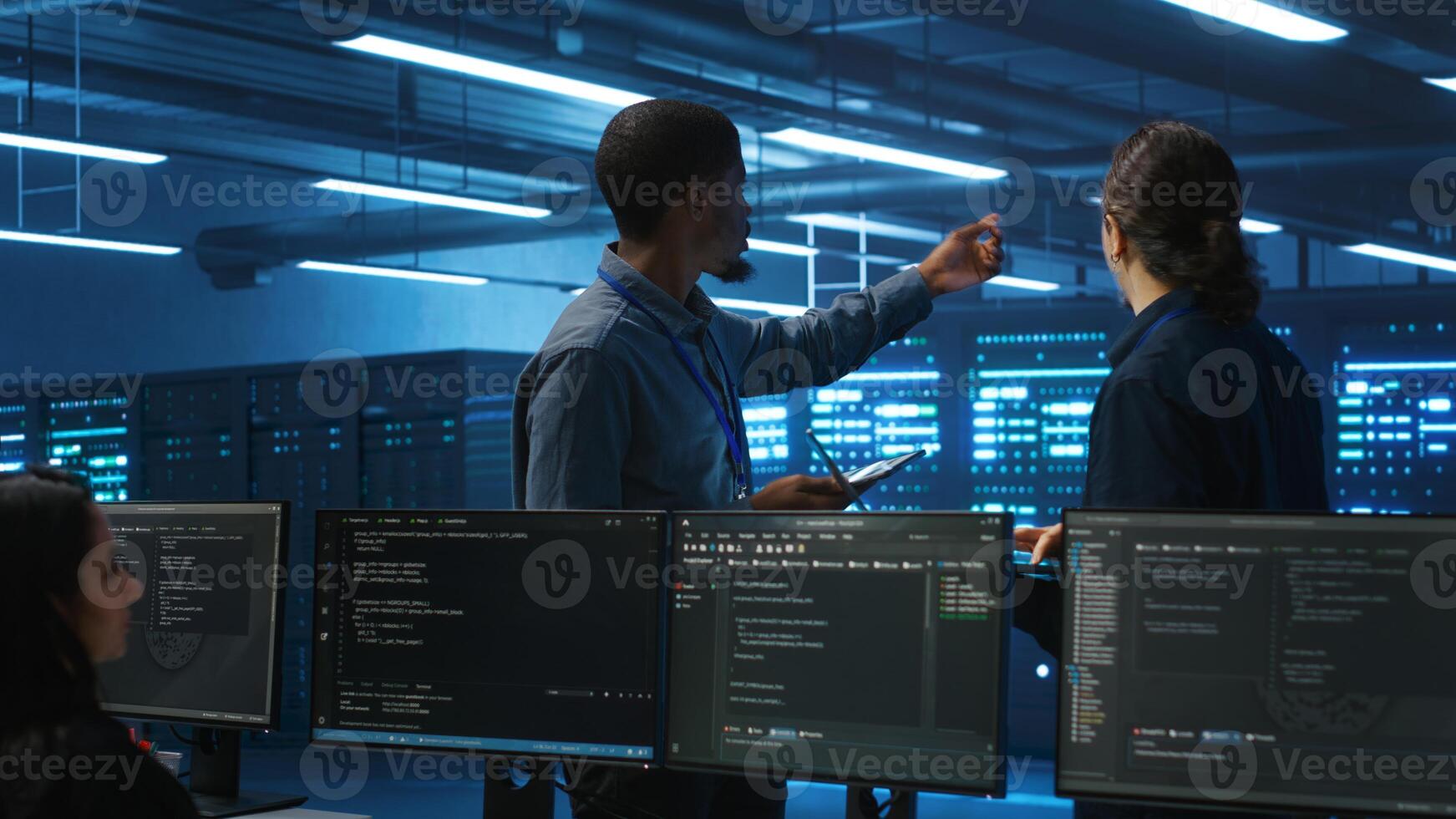 Multiracial team of technicians working in high tech server hub capable of storing vast amounts of data. Coworkers doing brainstorming, trying to troubleshoot servers controlling network resources photo