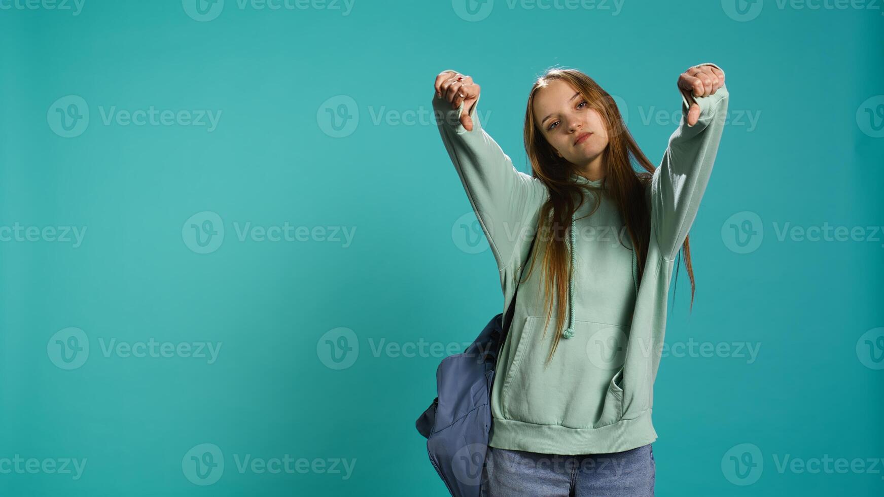 Frustrated woman showing thumbs down sign gesturing, disapproving and offering negative feedback. Disappointed girl doing dislike hand gesture, studio background, camera B photo