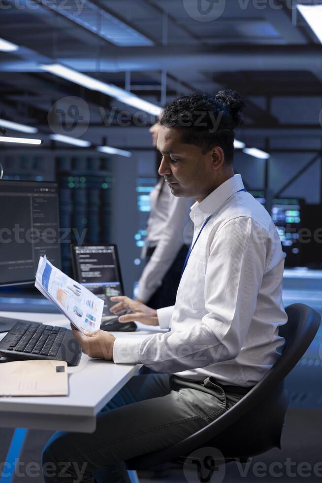 Serviceman in server hub checking documentation of supercomputers used for computationally intensive tasks such as scientific simulations or 3D rendering, doing annual equipment checkup photo