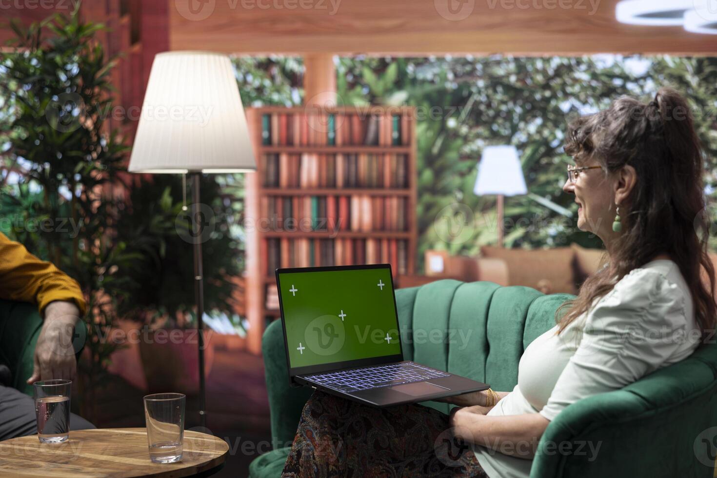 Mature people enjoying leisure time at home with green screen on laptop, laughing and chatting. Man and woman having fun together during retirement, wellness and companionship. photo