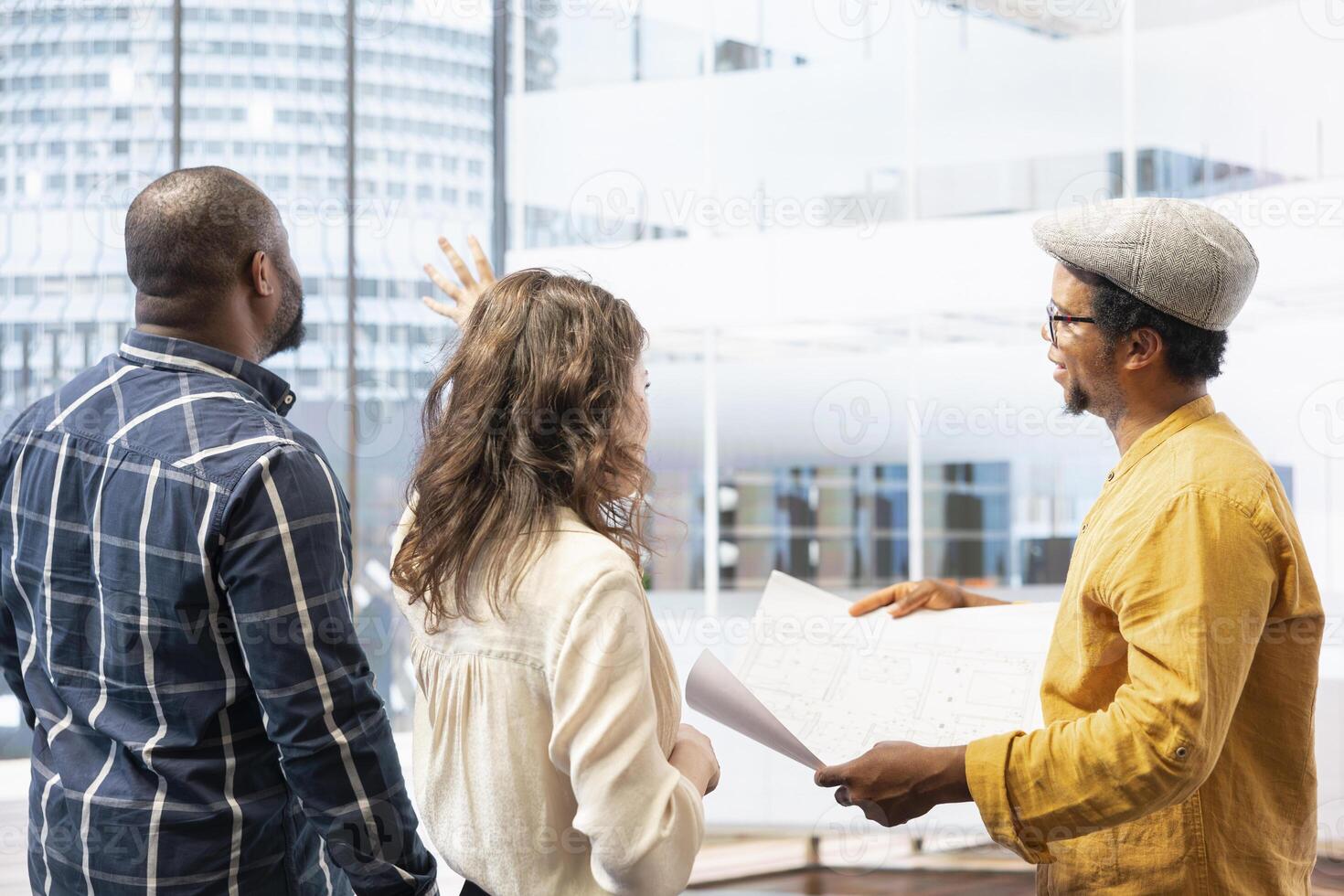 Clients and real estate agent on an office tour reviewing workspace design and blueprints, negotiating leasing contract for urban property. Planning corporate relocation in a building. photo