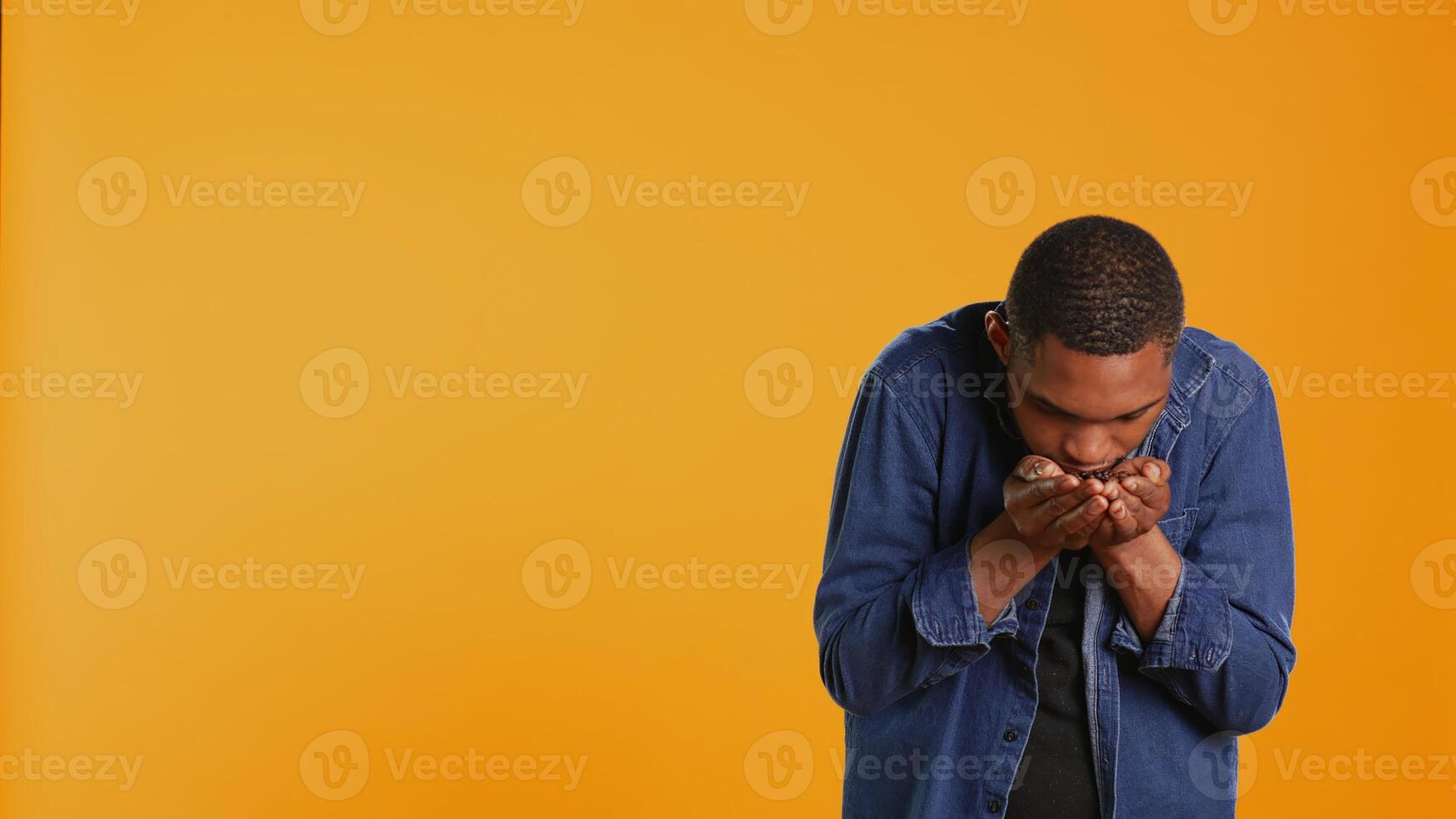 Coffee enthusiast looks at aromatic roasted beans against orange background, promoting cold brew at a coffee shop or cafeteria. Enjoying eco friendly delicious black seeds. Camera B. photo
