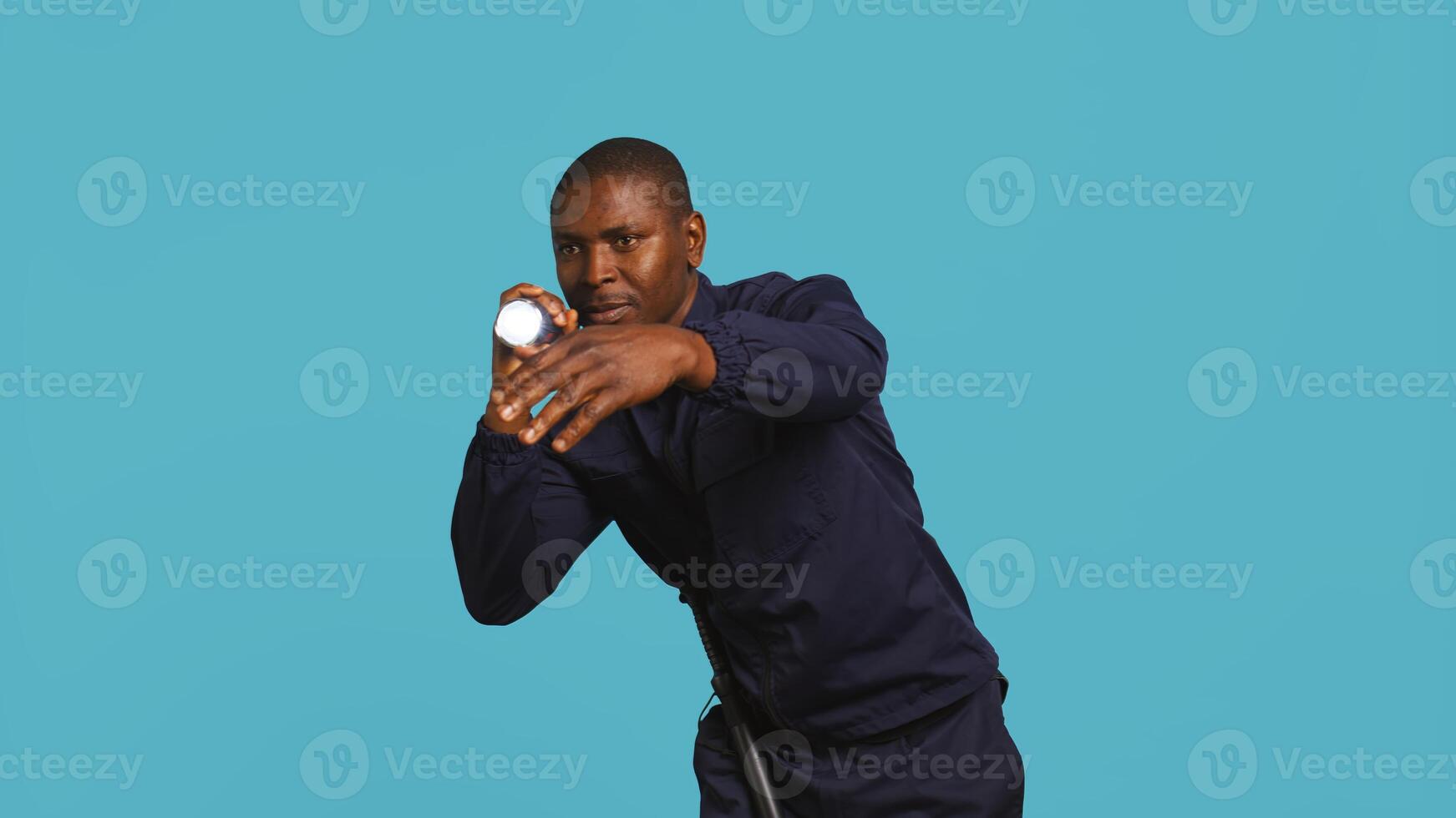 Portrait of security guard catching intruder with flashlight while overseeing premises. Private law enforcement worker calls over trespasser after detecting him with lantern, studio backdrop, camera B photo
