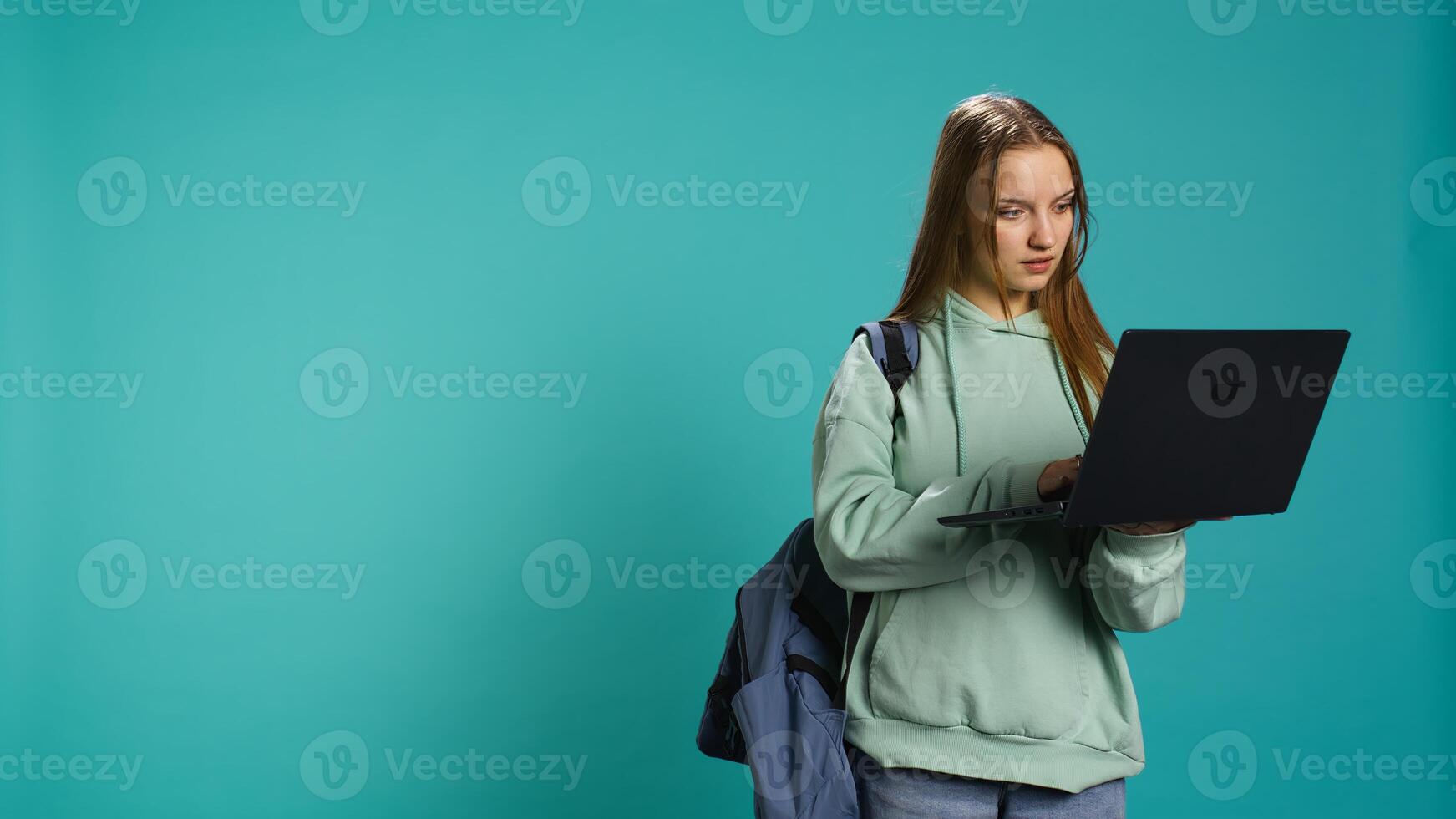Radiant woman opening laptop to prepare for school exam, isolated over blue studio background. Upbeat student using notebook to prepare for university classes, studio backdrop, camera B photo