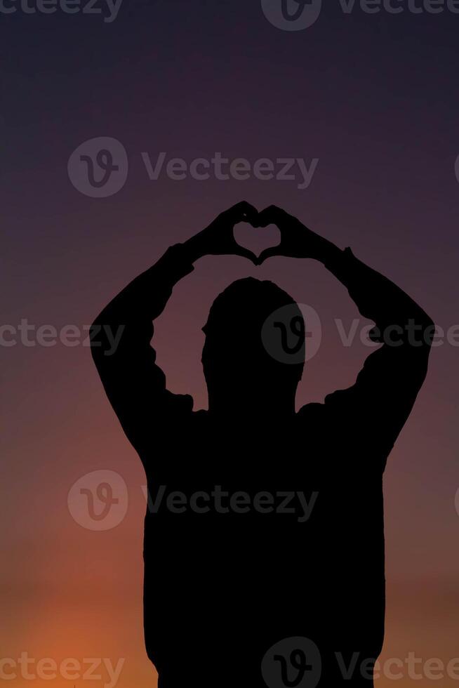 A silhouette of a young woman raising her hands above her head to represent a heart symbol signifying friendship, love and kindness. Heart symbol concept with the meaning of love and friendship. photo