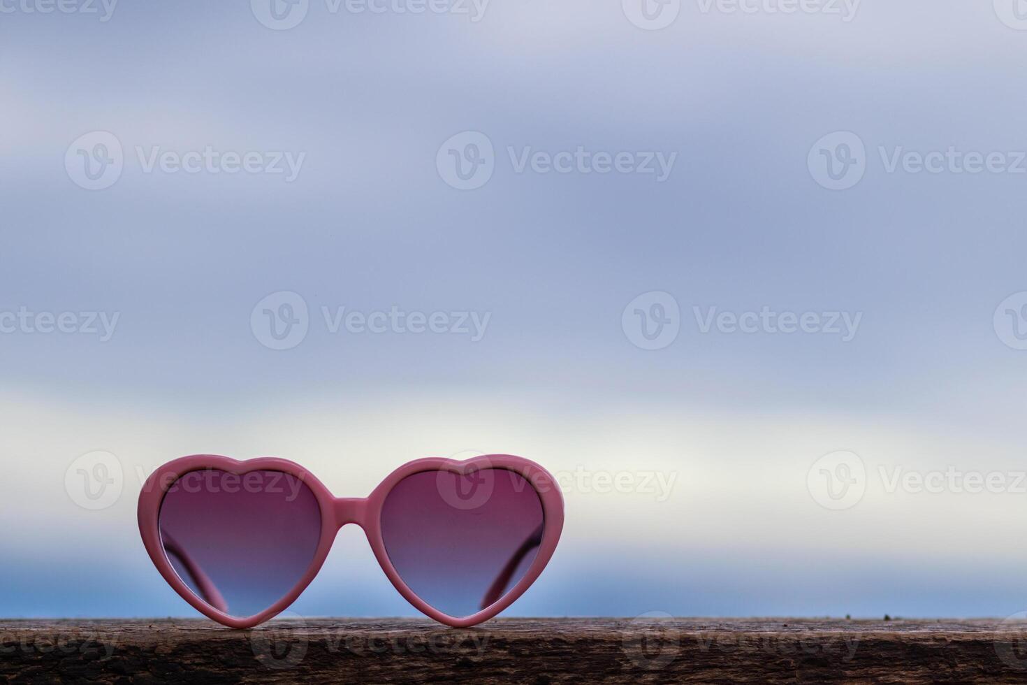 Heart-shaped sunglasses are placed on the balcony of the guest room against the blurred background of the sky. glasses are designed in pink heart to represent love and friendship between lovers. photo