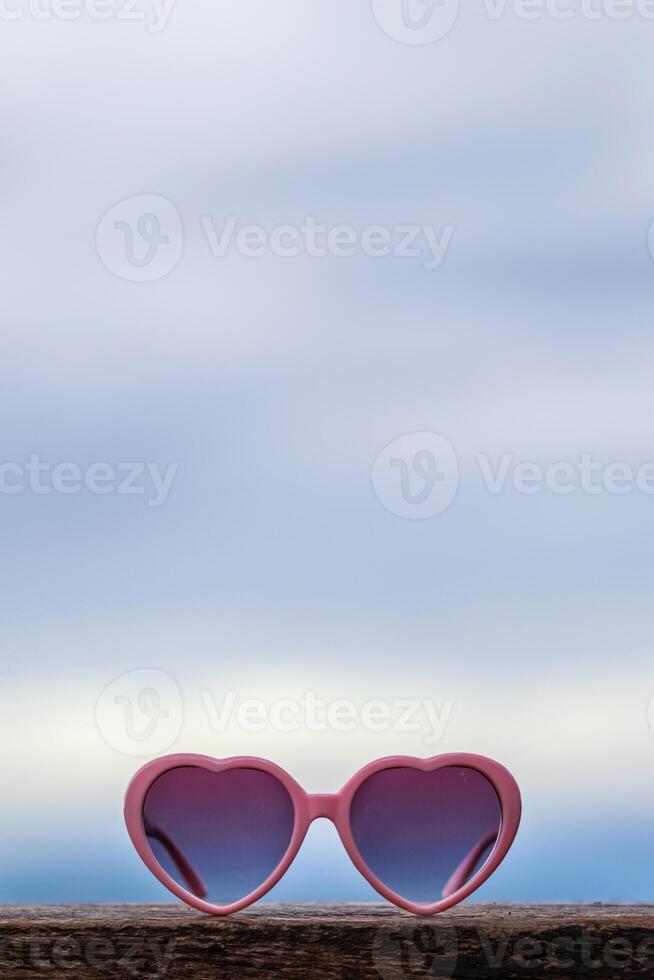 Heart-shaped sunglasses are placed on the balcony of the guest room against the blurred background of the sky. glasses are designed in pink heart to represent love and friendship between lovers. photo