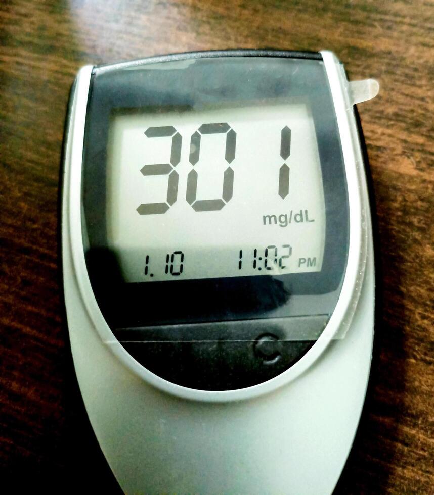 A close up of blood glucose meter with high sugar reading on wooden table photo