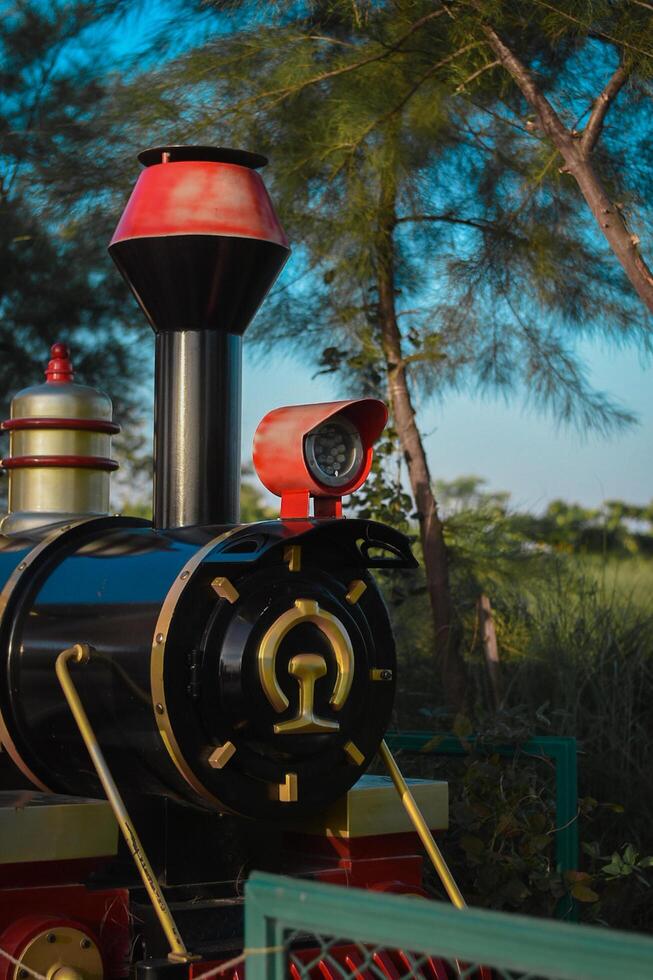 Discover the charm of a bygone era in this vibrant miniature train engine, nestled amidst the verdant splendor of a picturesque park. Timeless wonder and whimsy abound. photo