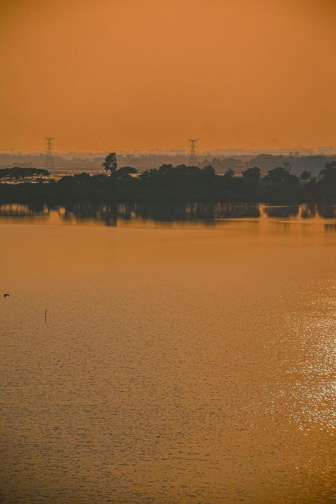As the sun paints the sky in warm hues, this tranquil scene invites us to embrace the beauty of the present moment. The still waters reflect the glow of a new dawn photo