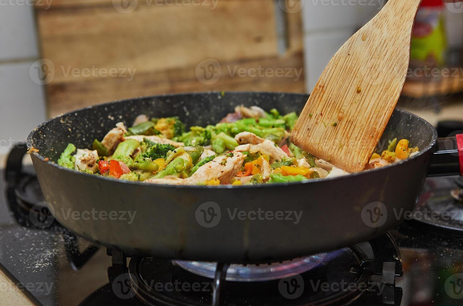 Colorful stir fry vegetables with chicken cooking in a pan on a gas stove in a home kitchen setting. photo