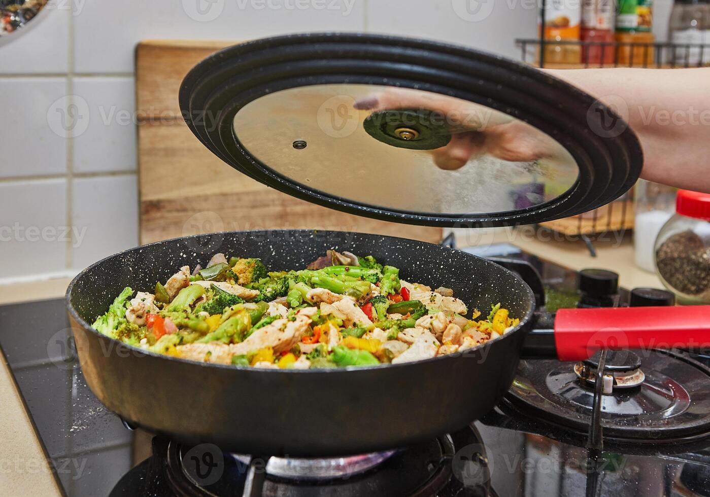 Colorful stir fry vegetables with chicken cooking in a pan on a gas stove in a home kitchen setting. photo