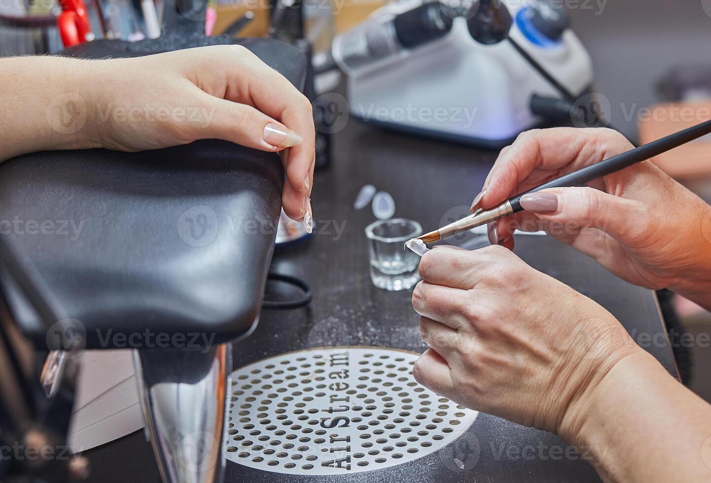 Close-up of a nail technician using a brush to apply gel to a nail in a salon setting photo
