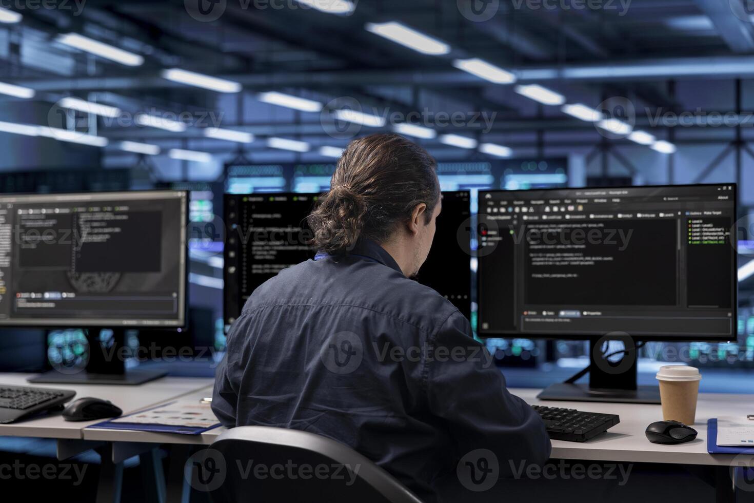 Programmer in server farm establishment ensuring data remains shielded from potential threats. Worker at computer desk safeguarding data center against unauthorized access photo
