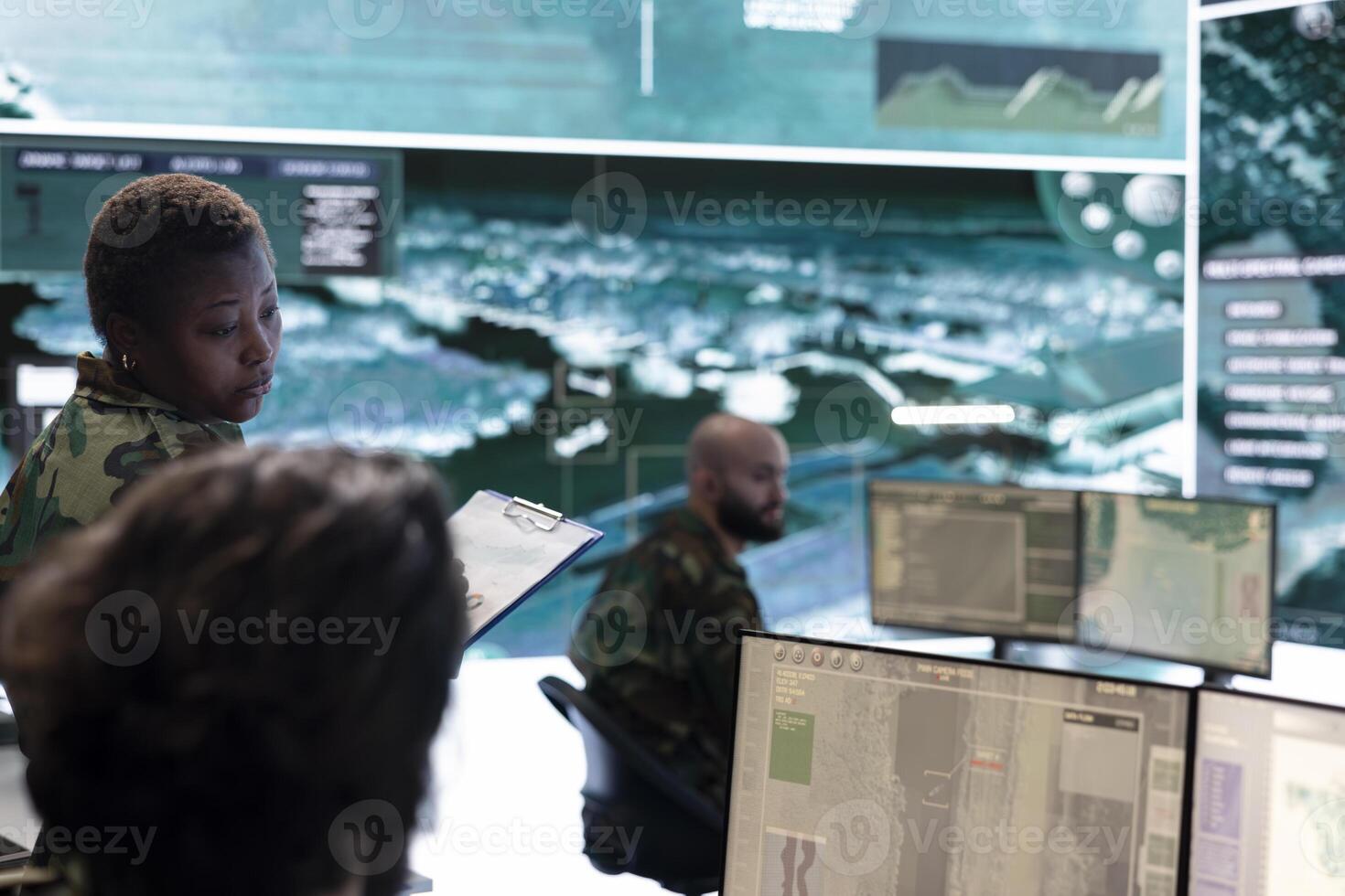 Female trooper checking real time battlefield data in command post control room, examining special missions and operations. Team of recruits interpret satellite imagery for reconnaissance. photo