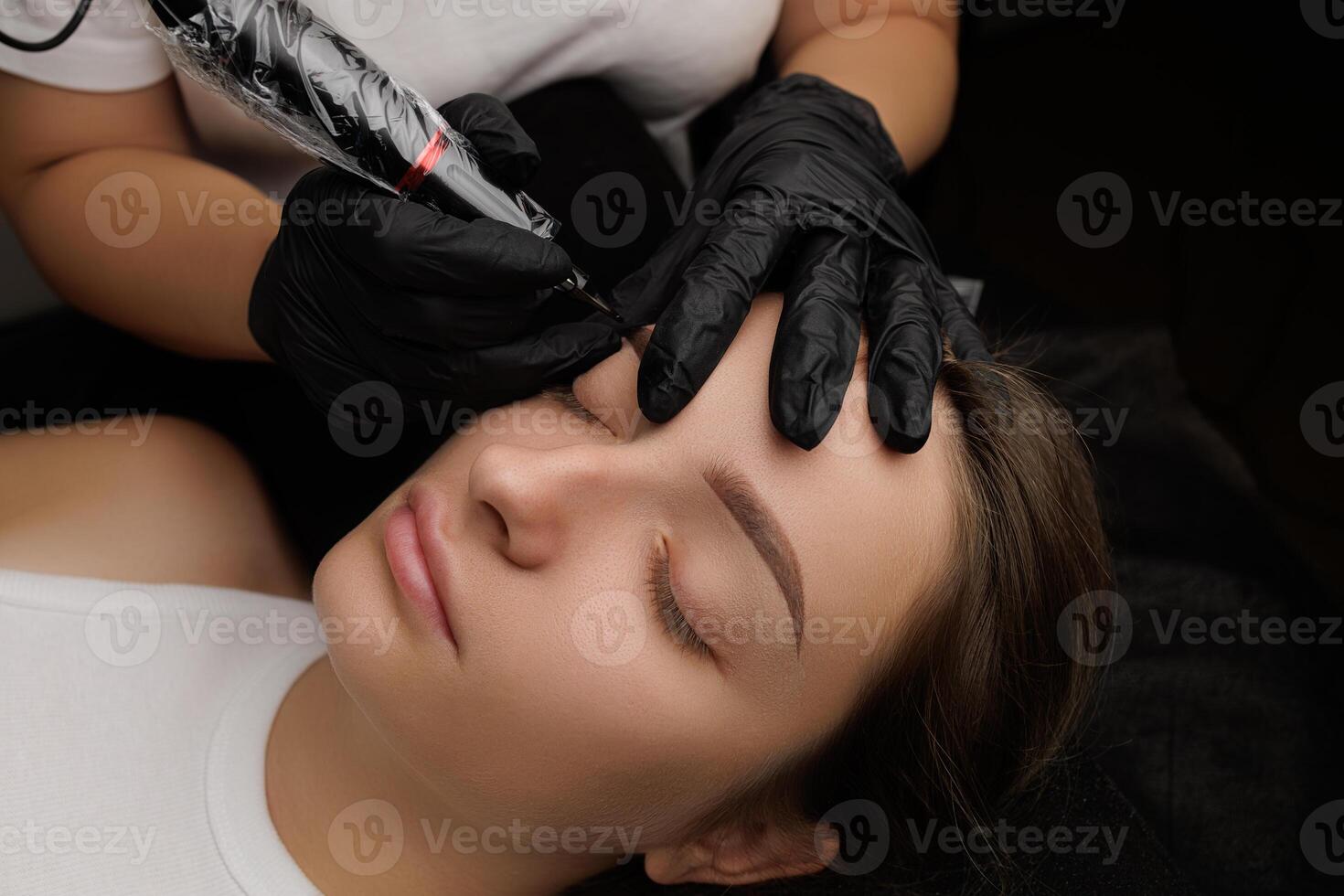 Close-up of the hands of the master who performs the procedure of permanent makeup of eyebrows view from above. Permanent eyebrow makeup PMU for brunettes photo