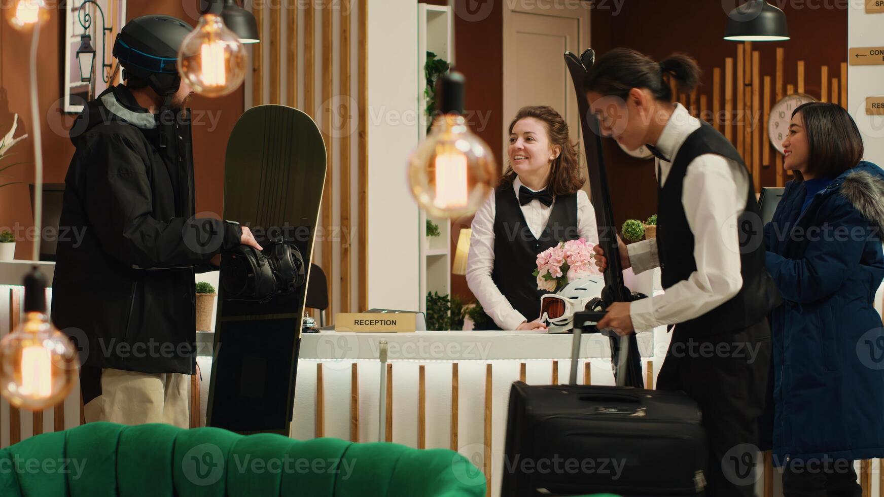 Two travelers enjoying winter vacation at alpine resort skiing and snowboarding for leisure activity. Couple standing at front desk reception of hotel lobby dressed in winter sport suits and gear. photo