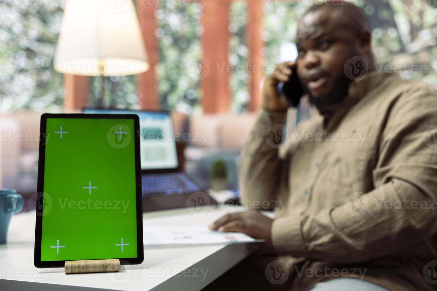 Business owner chats on phone call with shareholders next to green screen, transmitting data analytics sales reports from his home desk. Entrepreneur negotiates the funding with investors. photo
