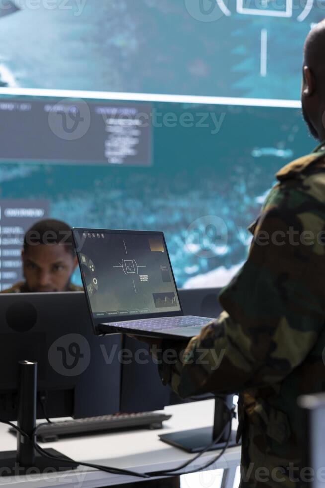 Cybersecurity specialist operates in a high tech military control center, monitoring surveillance footage and gathering intelligence for a new defense mission. Secret service activity. photo