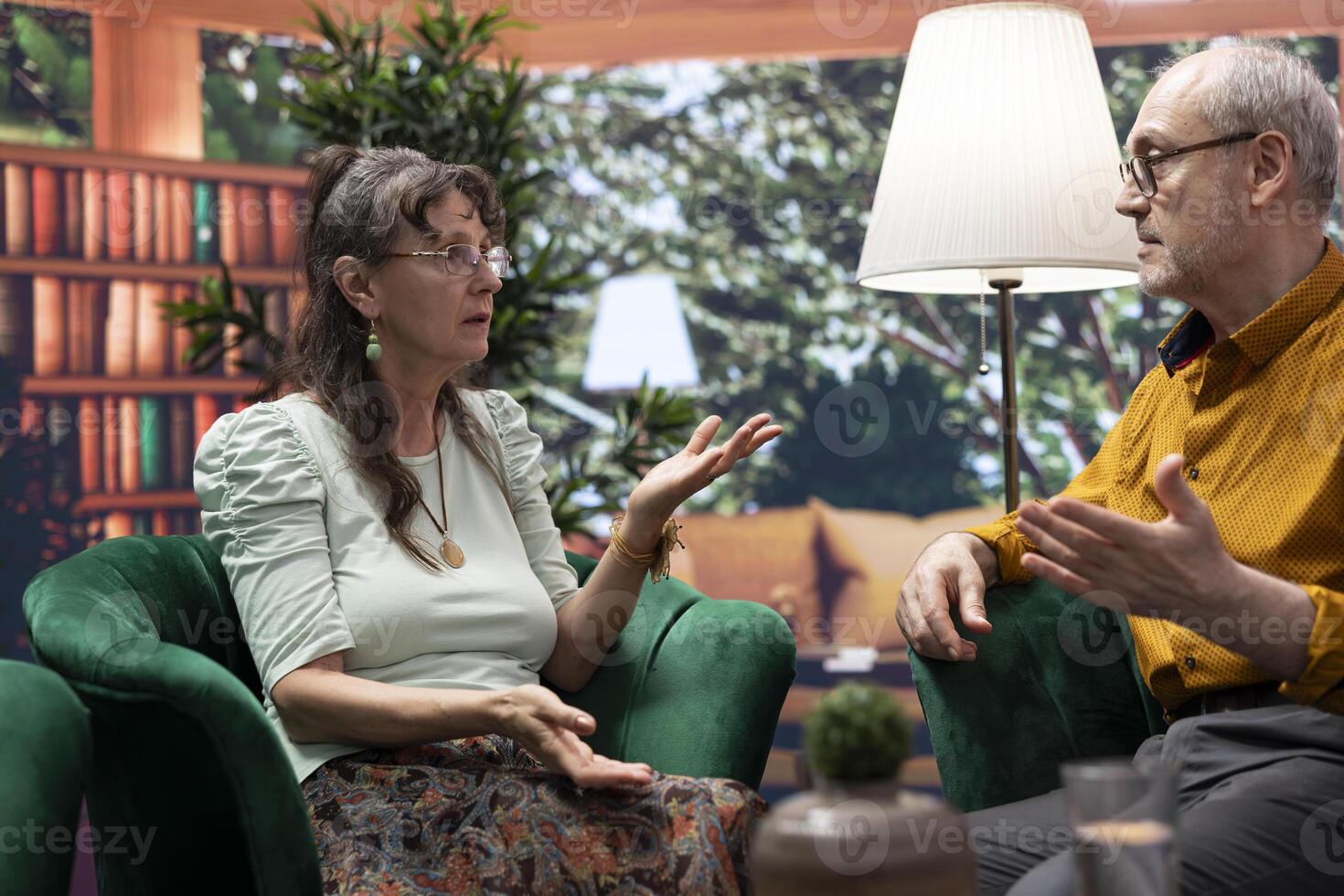 Elderly man and woman enjoying leisure free time at their home, engaging in a joyful conversation and laughing together. Relaxed and healthy aging people, wellness and companionship. photo