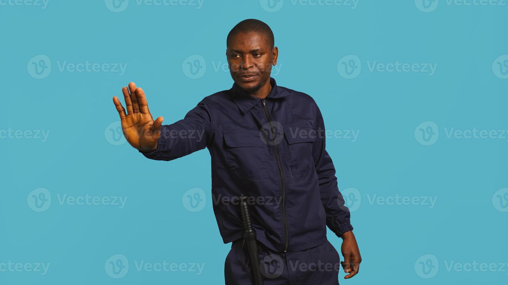 Portrait of security guard doing stop sign gesturing to intruder while overseeing premises. Private law enforcement worker showing halt hand gesture to trespasser, studio backdrop, camera B photo