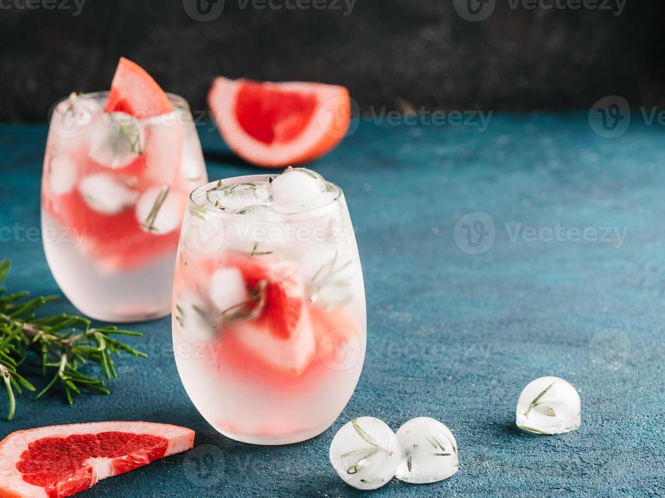 infused detox water or alcoholic or non-alcoholic cocktail with grapefruit and rosemary ice in glass on green and black cement background. healthy eating or holyday drink concept, copy space for text photo