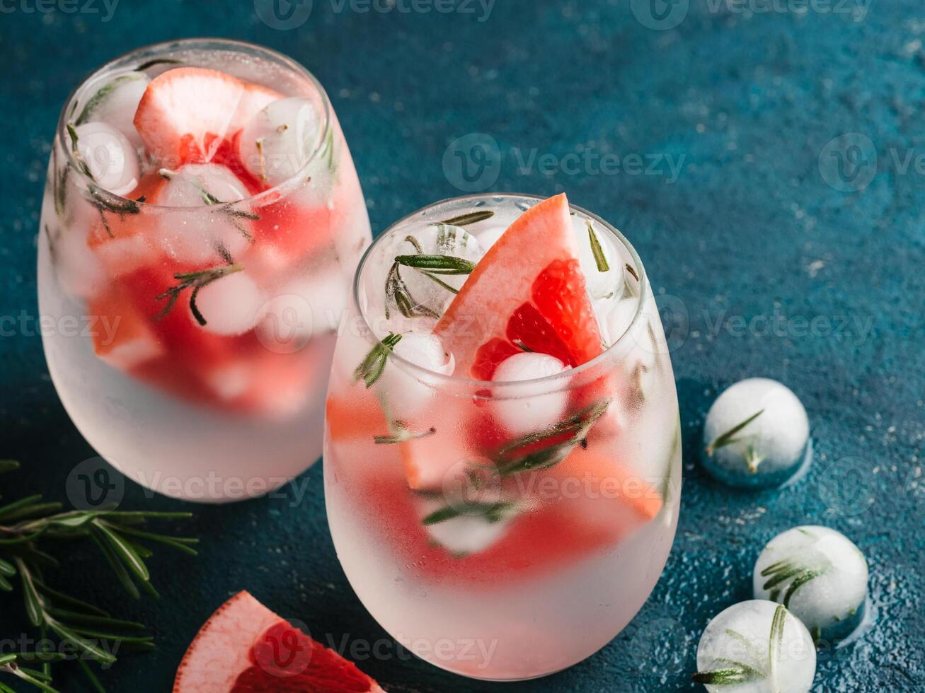 infused detox water or alcoholic or non-alcoholic cocktail with grapefruit and rosemary ice in glass on green cement background. healthy eating or holyday drink concept, copy space for text. photo