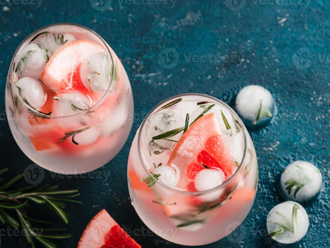 infused detox water or alcoholic or non-alcoholic cocktail with grapefruit and rosemary ice in glass on green cement background. healthy eating or holyday drink concept, copy space for text. photo