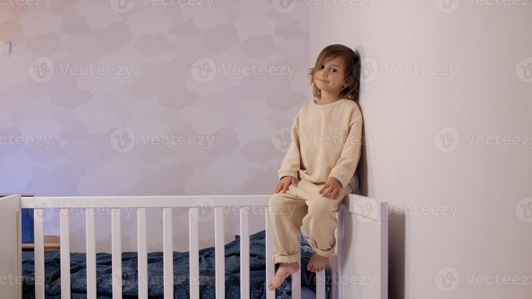 a little girl four years old sits in a bright room in a crib and smiles photo
