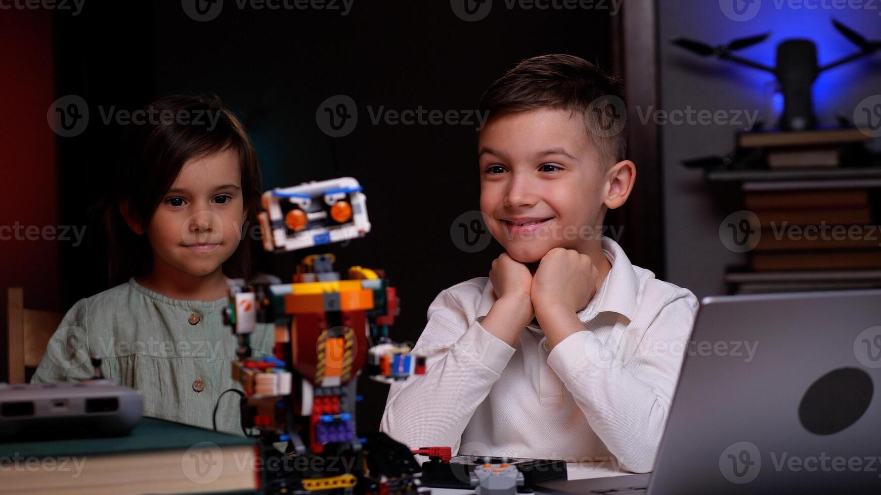 Two kids programming a robot from a laptop at home photo