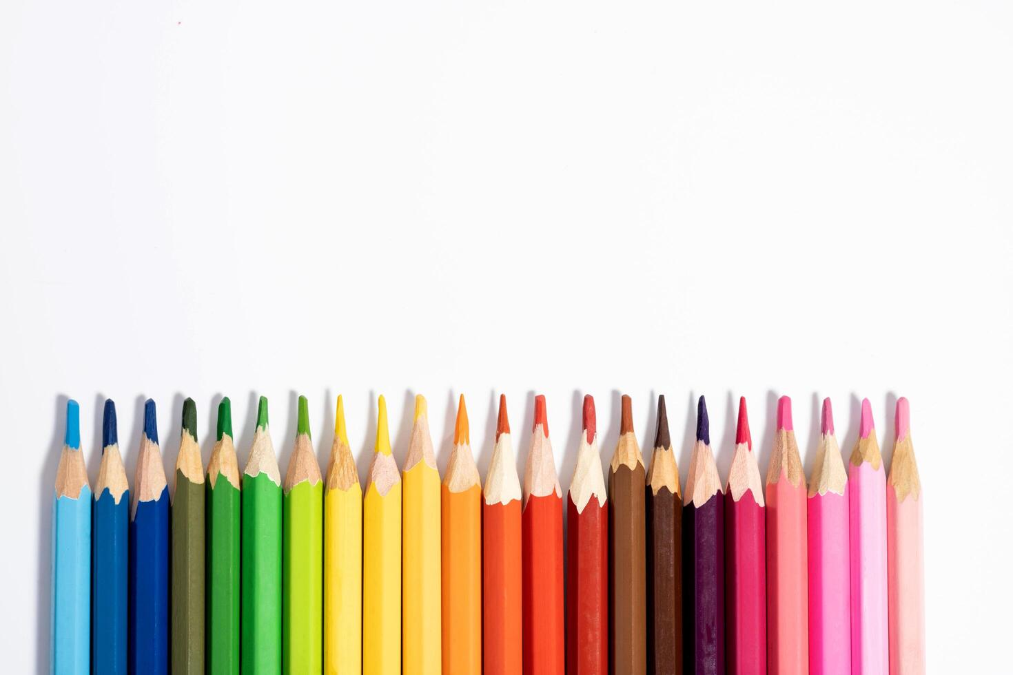 A set of colored pencils are displayed in a row below a white background with the leads facing up photo