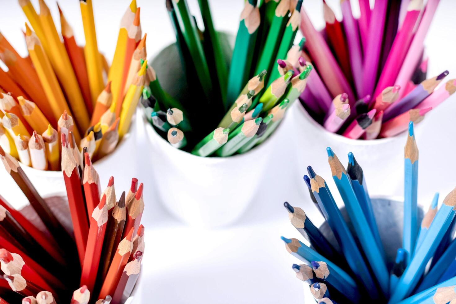 Sets of colored pencils arranged by color in white cups on a white background top view photo