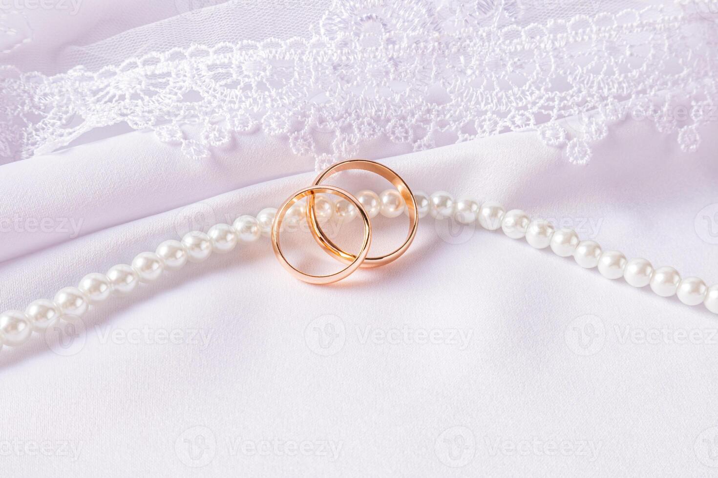 Two gold wedding rings lie on a string of pearl beads. on a white satin background with an embroidered veil. The concept of the wedding. Front view. photo