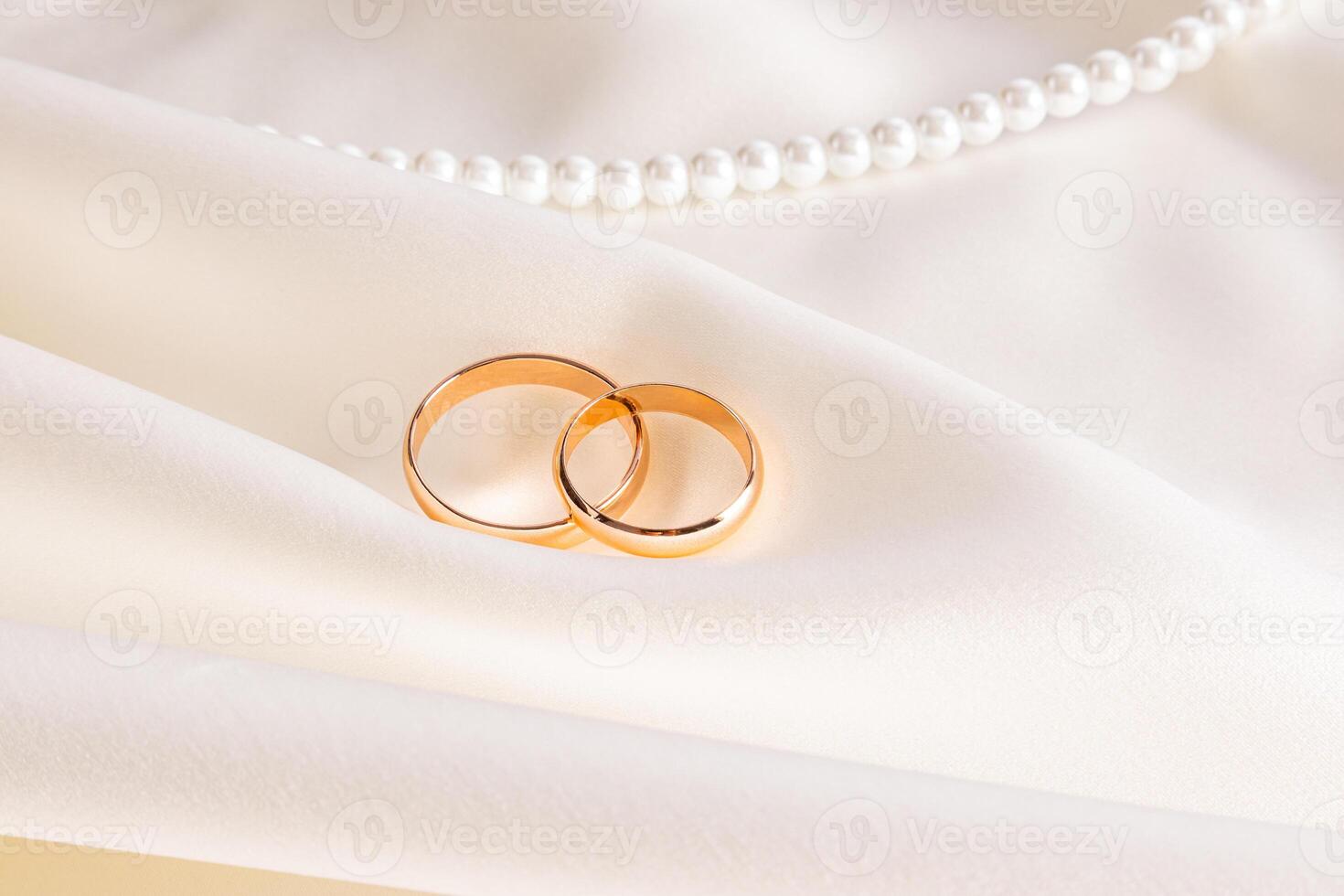 Two classic gold wedding rings on a beige satin background with beautiful pleats and a string of pearl beads. Wedding design concept. invitation. photo
