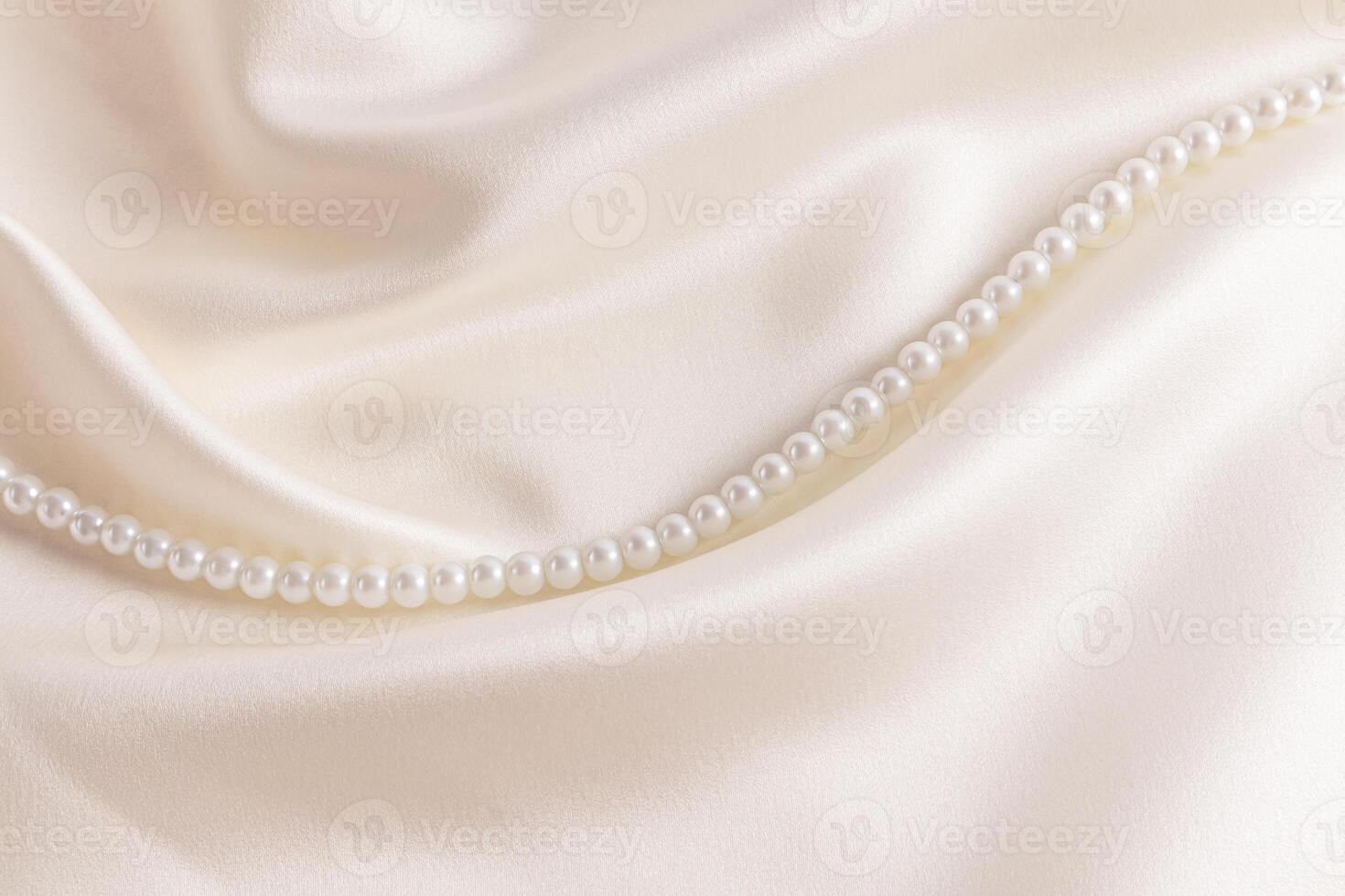 Chic cream-colored satin with a string of pearl beads among the soft waves of fabric. Wedding holiday backdrop for design. A copy space photo