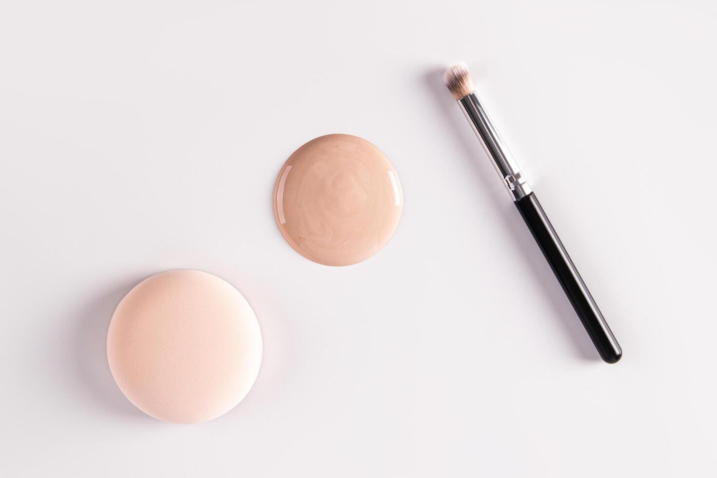 A large round spot of foundation powder in a natural tone, a cosmetic round sponge and a makeup brush. top view. white background. photo